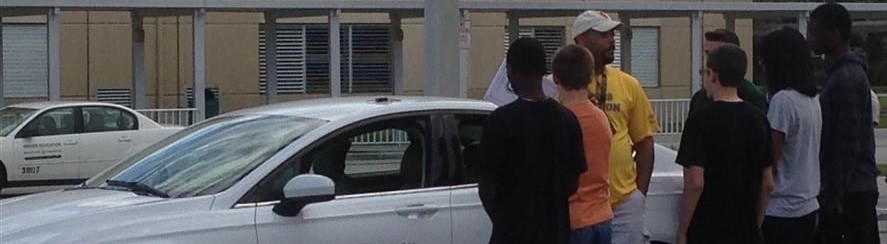 Driver's Ed teacher speaking to students near white driver's ed car Driver's Ed teacher speaking to students near white driver's ed car